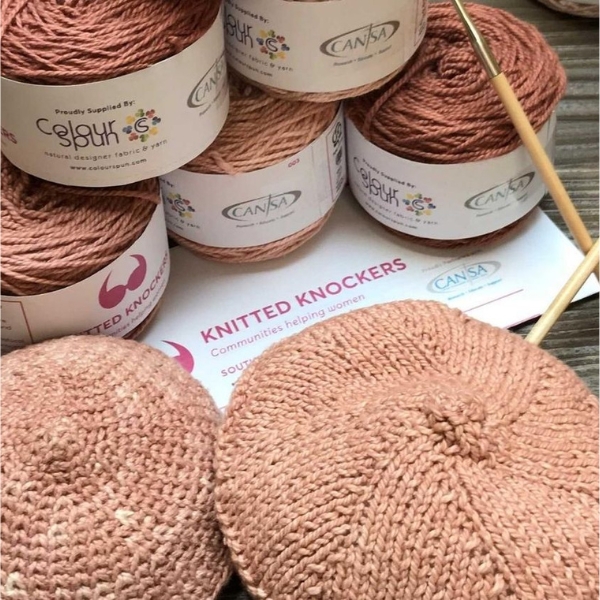 ColourSpun cotton yarn with CANSA and Knitted Knockers branding, two completed hand-knitted breast prostheses and wooden knitting needles