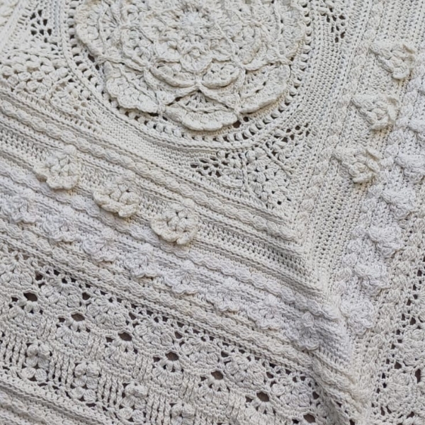 Angled close up of Mixology Edition 6 by Hooked on Sunshine, crocheted in Cotton Scintilla DK, showing the raised floral centre medallion, scattered bobble flowers and diagonal lace stitch detail