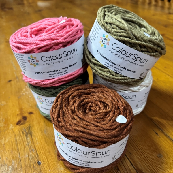 ColourSpun Pure Cotton Super Chunky Smooth yarn cakes in pink, sage green, natural cream and rust, stacked with a rust coloured cake in the foreground