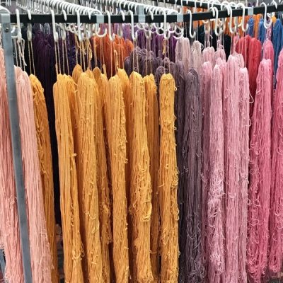 Freshly dyed yarn skeins hanging to dry on a rack in the ColourSpun studio, in shades of orange, peach, purple and pink