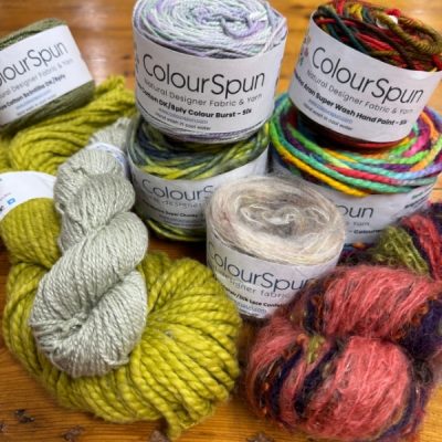 A selection of ColourSpun hand dyed natural yarns including merino, mohair and cotton in various weights, displayed on a wooden surface